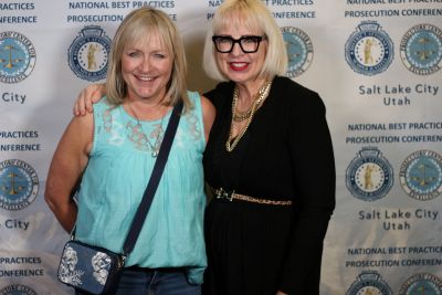 Two people stand in front of a backdrop at the 2024 National Prosecution Best Practices Conference.