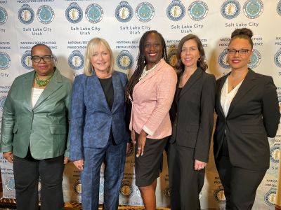Five people stand in front of a backdrop at the 2024 National Prosecution Best Practices Conference. 