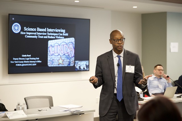 A speaker at the PERF Prosecutor Police Collaboration Meeting stands in front of a television screen where a presentation titles "Science Based Interviewing is shown. 